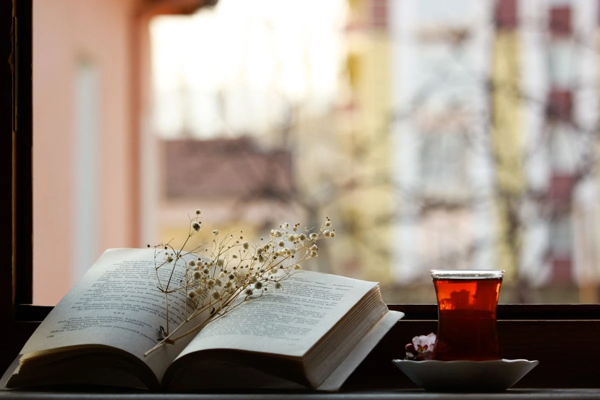 Libro abierto y taza de té junto a una ventana